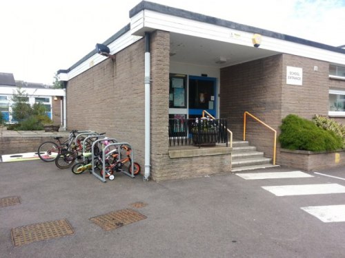 Stojaki na rowery przy szkole podstawowej z przypiętym rowerkiem z kołami bocznymi.