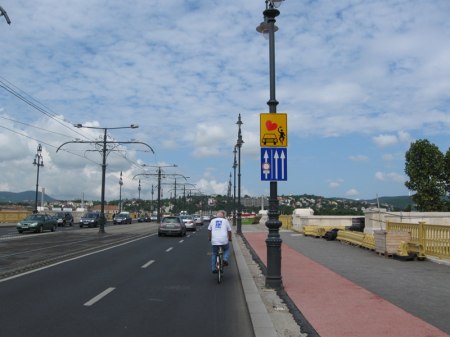 Znak zachęcający do wzajemnej uprzejmości na jezdni. Obok budowa drogi rowerowej wytyczonej z chodnika - niestety lampy w skrajni.