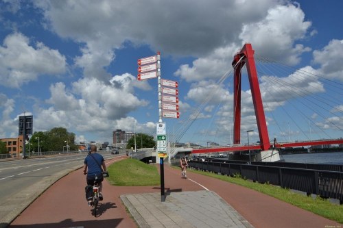 Dojazd do Willemsbrug. Na słupku są drogowskazy do dzielnic Rotterdamu, sąsiednich miast, tabliczka szlaku rowerowego LF oraz systemu rowerowych punktów węzłowych.